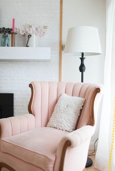 a pink chair sitting in front of a white brick wall with a lamp on top of it