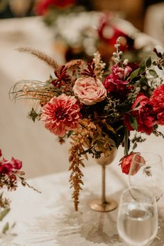 a vase filled with lots of flowers on top of a white tablecloth covered table