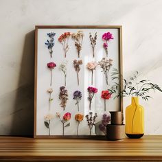 an arrangement of dried flowers displayed in a wooden frame on a table next to a yellow vase