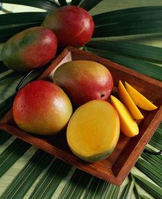 two mangoes and three pieces of fruit in a wooden tray