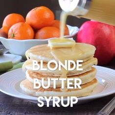 a stack of pancakes sitting on top of a white plate next to oranges and apples