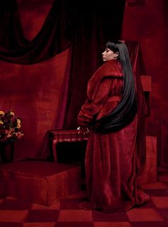 a woman in a red fur coat standing next to a table with flowers on it