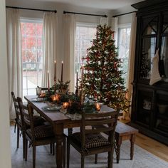 a dining room table set for christmas with candles on it and a tree in the background