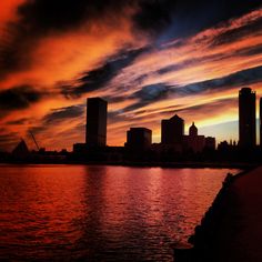 an orange and blue sky over the water with buildings in the backgrouds