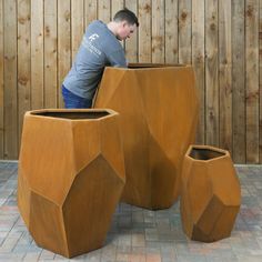 a man leaning over a large wooden vase on top of a brick floor next to two planters