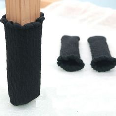 a pair of black knitted mittens next to a wooden stick on a white surface