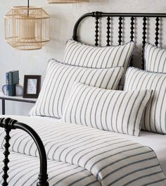 a bed with white and blue striped pillows on it's headboard next to a lamp