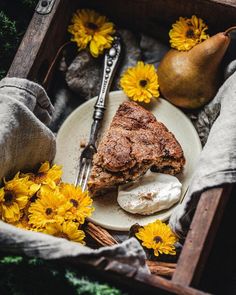 a piece of pie sitting on top of a white plate next to yellow flowers and a pear