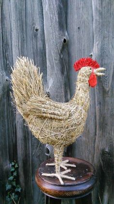 a chicken made out of straw sitting on top of a wooden stool next to a fence