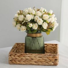 a green vase with white flowers in it sitting on a wicker tray next to a window