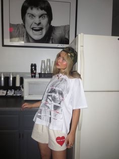 a woman standing in front of a refrigerator with a poster on the wall behind her