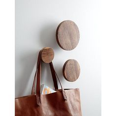 a brown leather tote bag hanging on a wall with three wooden circles above it