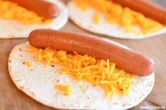 two hot dogs on tortilla shells with shredded cheddar cheese toppings