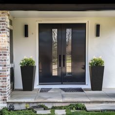 two planters on the front steps of a house with black doors and sidelights