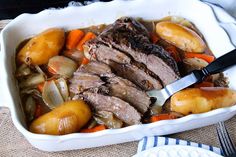 a white dish filled with meat, potatoes and carrots on top of a table