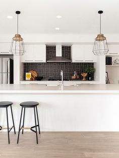 two stools sit at the bar in this modern kitchen with white cabinets and black tile backsplash