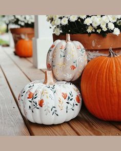 three painted pumpkins sitting on a wooden table next to potted plants and flowers