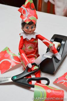 an elf is sitting on top of a stapler with scissors and wrapping paper next to it