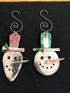 two metal snowmen with hats and scarfs hanging from hooks on a black surface