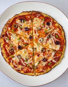 a pizza cut into eight slices on a white plate with green peppers and olives