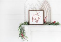 a white mantle with a framed holiday sign and greenery