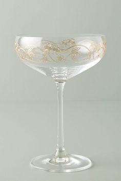 an empty wine glass sitting on top of a white tableclothed flooring with gold leaf designs