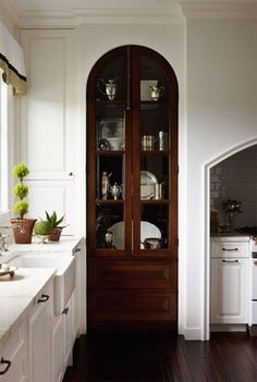 a kitchen with white cabinets and wood flooring next to a large glass doored cabinet