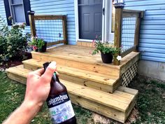 someone is holding a bottle of beer in front of a house with flowers on the steps