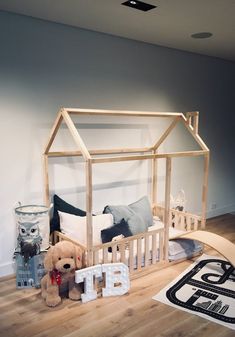 a wooden dollhouse bed with a teddy bear in the middle and other toys on the floor