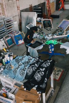 a man is working on some clothing in a room full of other items, including jeans and t - shirts