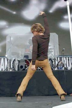 a man in brown shirt and tan pants standing on stage with his arms raised up