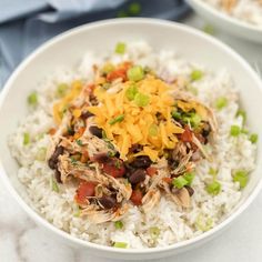 a white bowl filled with rice topped with shredded cheese and black beans, garnished with green onions