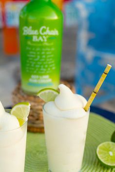 two glasses filled with ice cream and limes on a plate next to a bottle