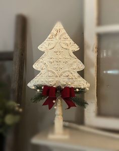 a small white christmas tree with red bows on it's head sitting on a shelf