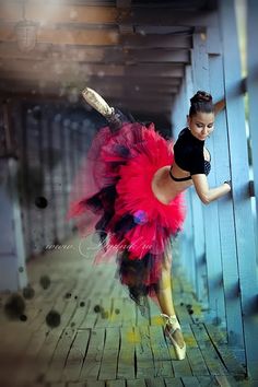 a woman in a black top and pink tutu is dancing on a wooden floor