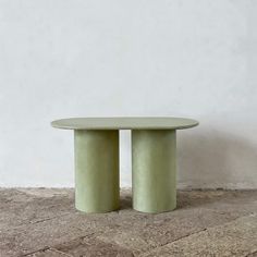 two green round tables sitting on top of a stone floor next to a white wall