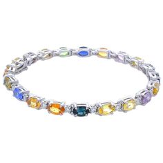 The colors in this natural sapphire bracelet make it one to be remembered. A total of 20 oval cut, prong set, sapphires that measure 6x4MM each and weigh a total of 11.72 carats adorn this stunning bracelet. The sapphires are sourced from Sri Lanka; their colors, clarities, and transparencies are excellent. The color are royal blue, lilac, golden yellow, blush green, and intense orange. Each sapphire alternates with 20 sparkling round brilliant cut diamonds that total 0.84 carats and measure 2.2 Argentium Silver Jewelry, Sapphire Bangle, Black Diamond Bracelet, Yellow Gold Bangle, Modern Bracelets, White Gold Sapphire, Multi Sapphire, Bracelet Display, White Gold Bracelet