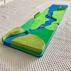 a close up of a wooden toy boat on a white tablecloth with blue water and green land