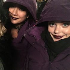 two women wearing purple coats and black scarves are posing for the camera with one woman's face covered in dark lipstick