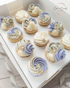 twelve cupcakes with white and blue frosting in a box on a table