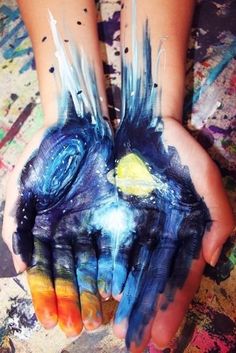 two hands are painted with different colors and shapes, one is holding the other's hand