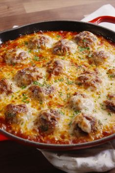 a pan filled with meatballs and cheese on top of a wooden table next to a napkin