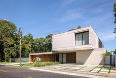 a modern house sits on the corner of a street in front of some trees and bushes