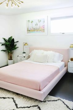 a pink bed with white sheets and pillows in a bedroom next to a potted plant