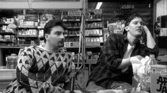 two men sitting at a table in a store talking to each other while one man holds his head up