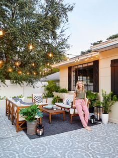 a woman sitting on top of a wooden bench next to a table with chairs and potted plants