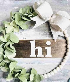 a wooden sign with the word hi on it next to some green leaves and beads