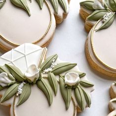 decorated cookies with green leaves and white flowers are on a table next to each other