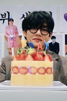 a man holding a cake with candles in front of his face and photos on the wall behind him