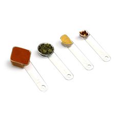 four spoons are lined up next to each other with spices in them on top